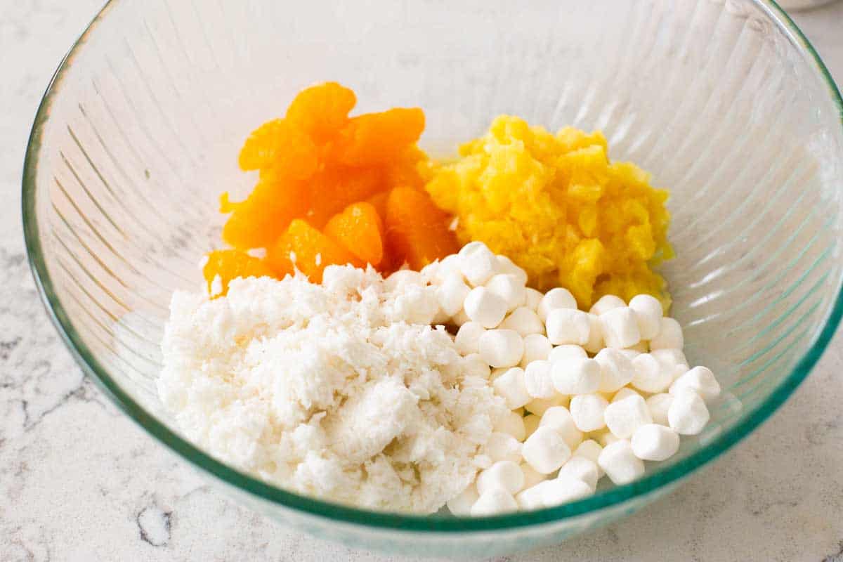 A mixing bowl has all the ambrosia ingredients ready to mix.