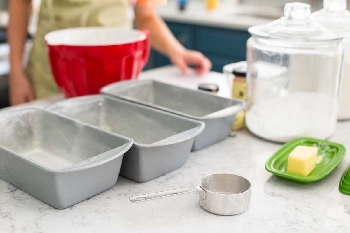 The baking pans are lined up on the counter next to butter and the ingredients.