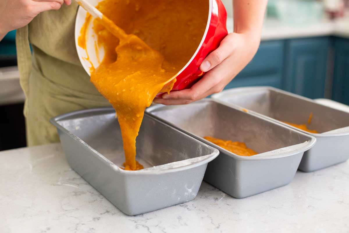 The pumpkin bread batter is being poured into 3 baking pans.