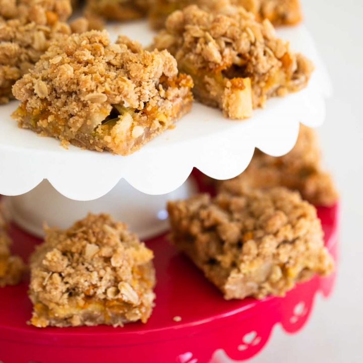 Tiered cake plate serves squares of apple crisp bars with an oat crumble topping and butterscotch chips.