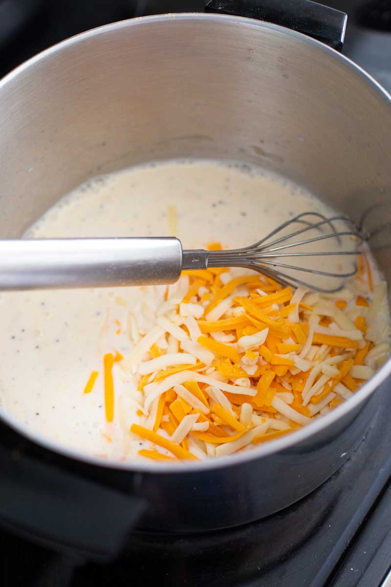 A pot has milk and shredded cheese to make homemade mac and cheese.