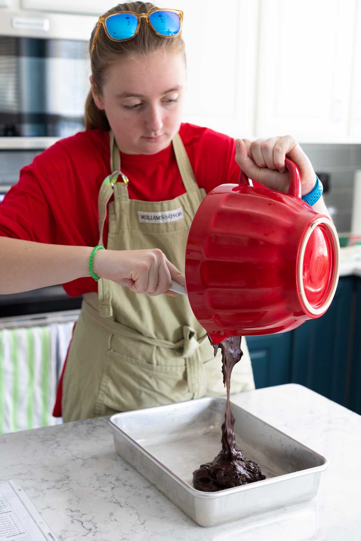 A young girl scrapes prepared brownie batter into a baking pan.