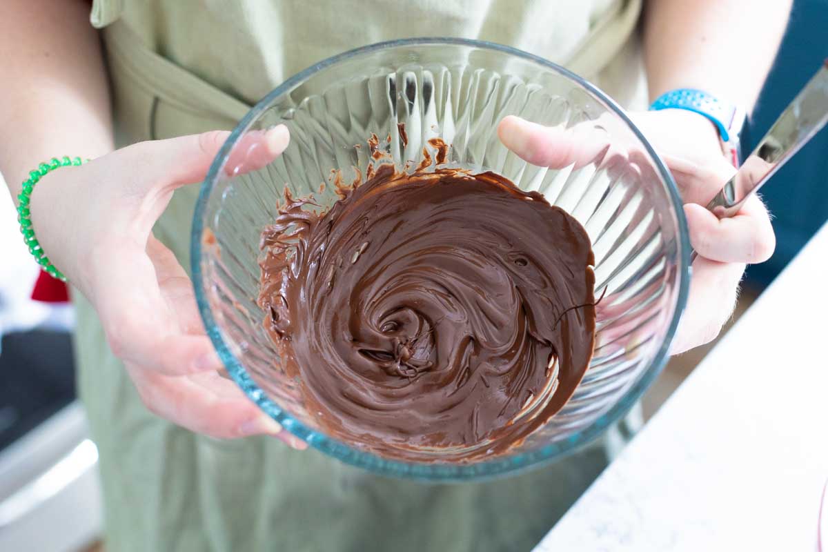 A girl's hands show a glass bowl filled with melted chocolate chips.