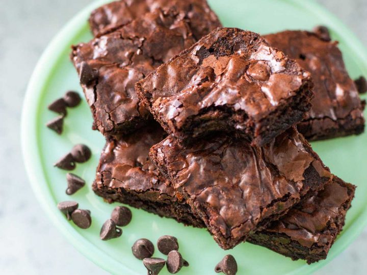 A round platter of a pile of chocolate brownies with a bite taken out of the one on top and a sprinkle of chocolate chips to the side.