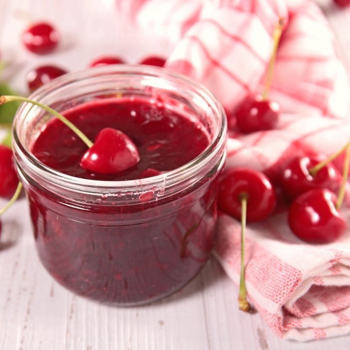 A mason jar of cherry jam has fresh cherries on a towel.