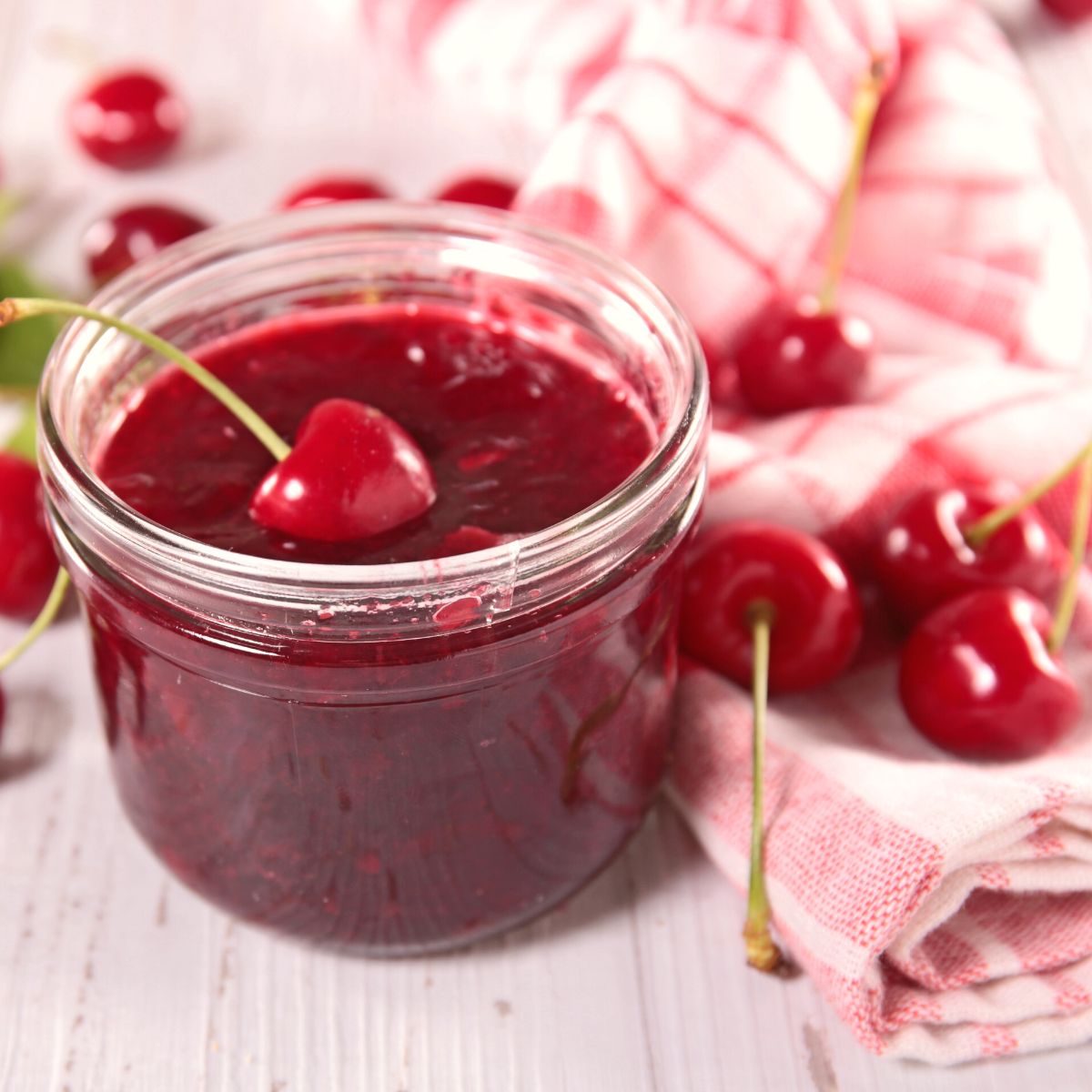 A mason jar of cherry jam has fresh cherries on a towel.