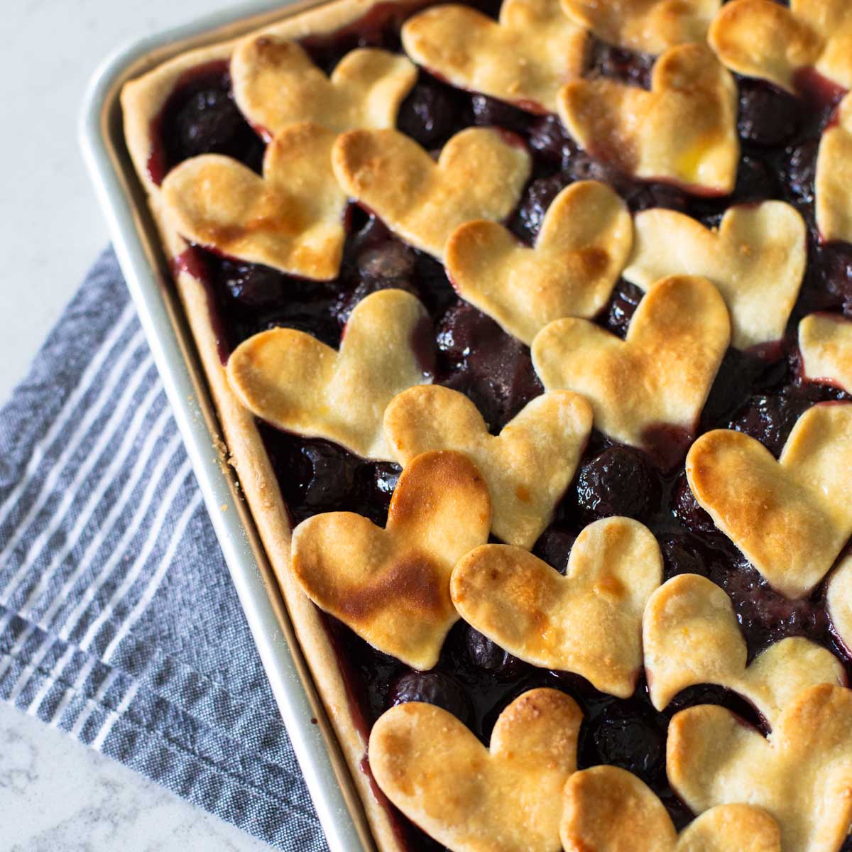 A cherry slab pie sits in a metal baking pan and has heart-shaped cut outs for the top crust.