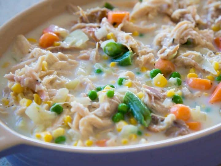 A purple baking dish has the chicken pot pie filling ready to be topped with crust and baked.