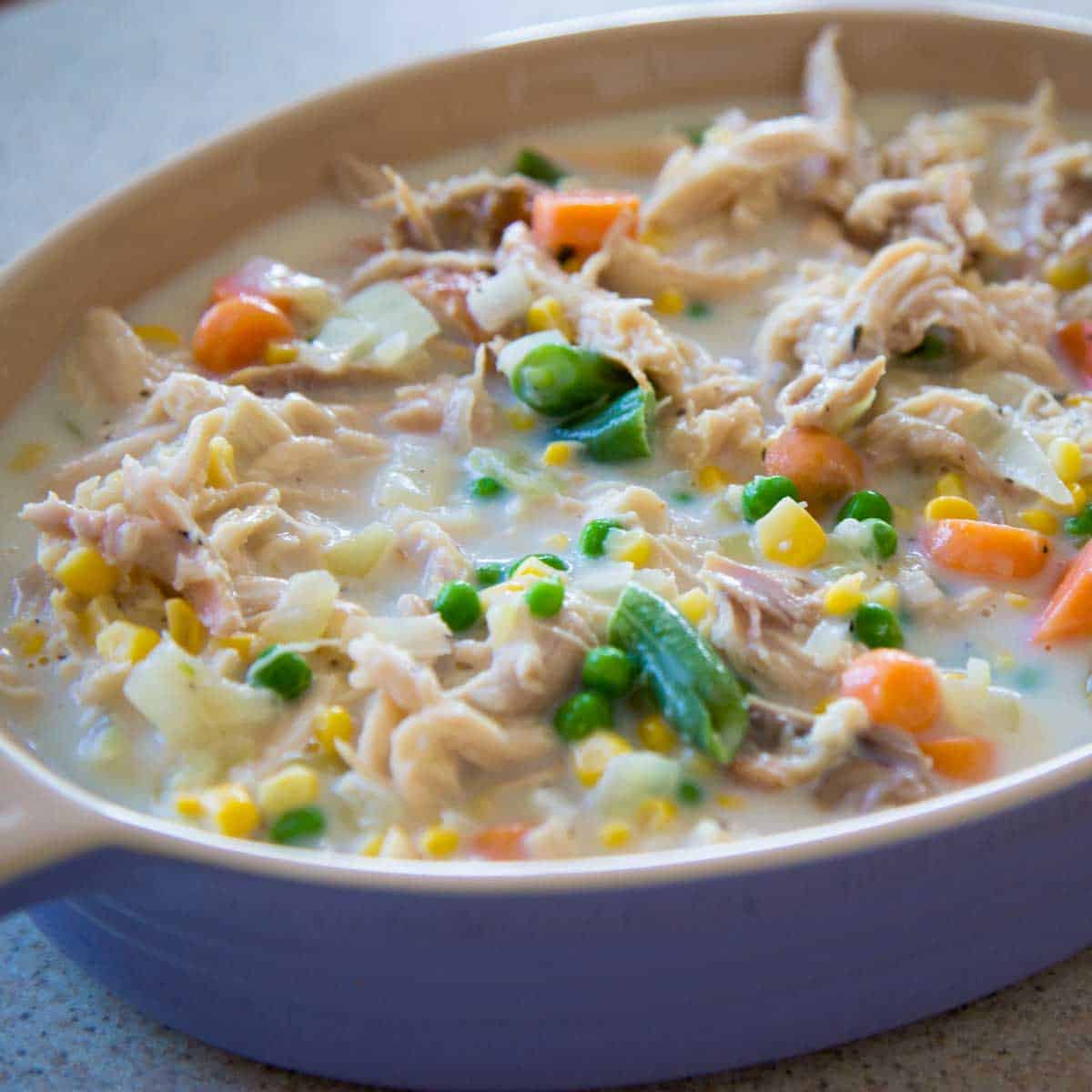 A purple baking dish has the chicken pot pie filling ready to be topped with crust and baked.