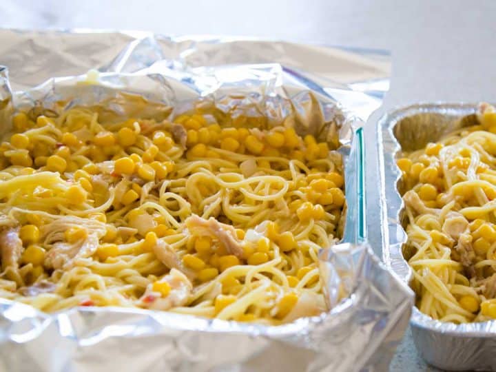 A square pan of chicken spaghetti is ready to be frozen in aluminum foil wrap.