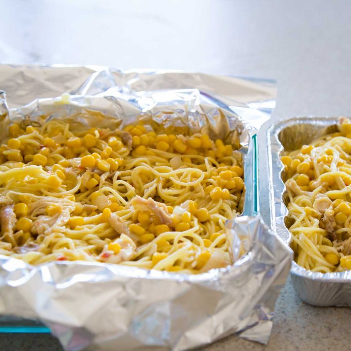 A square pan of chicken spaghetti is ready to be frozen in aluminum foil wrap.