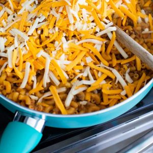 A large skillet is filled with chile mac covered in shredded cheese.