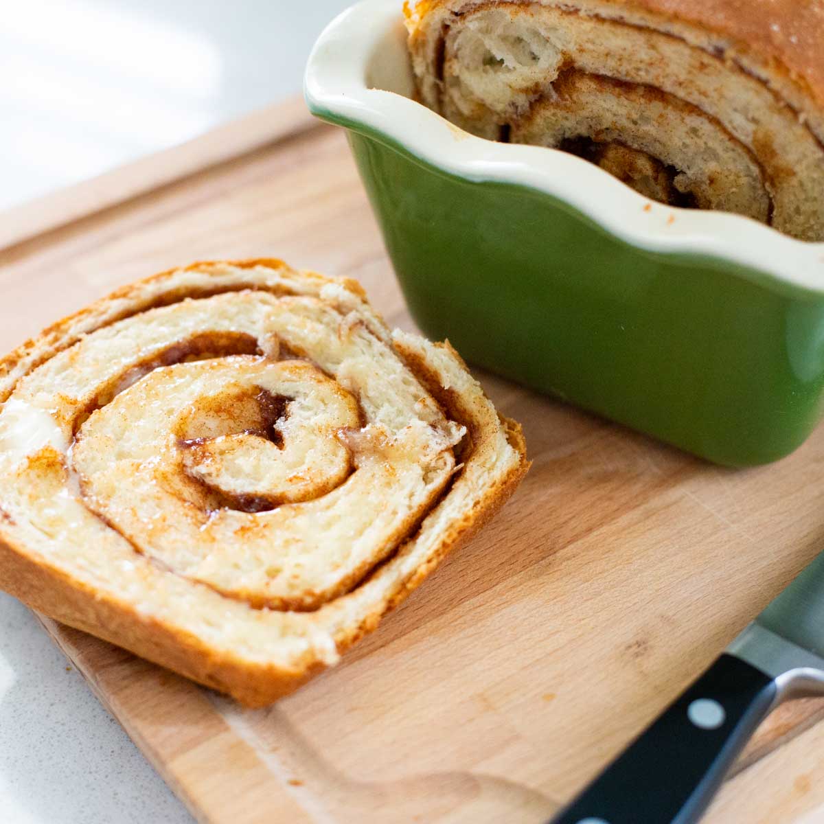 A slice of cinnamon swirl bread sits on a cutting board next to the bread pan it came from.