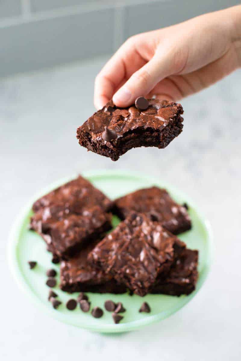 A young child's hand is holding a brownie with a bite taken out.