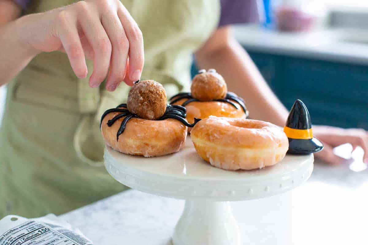 A girl is putting a decoration on a Halloween donut.