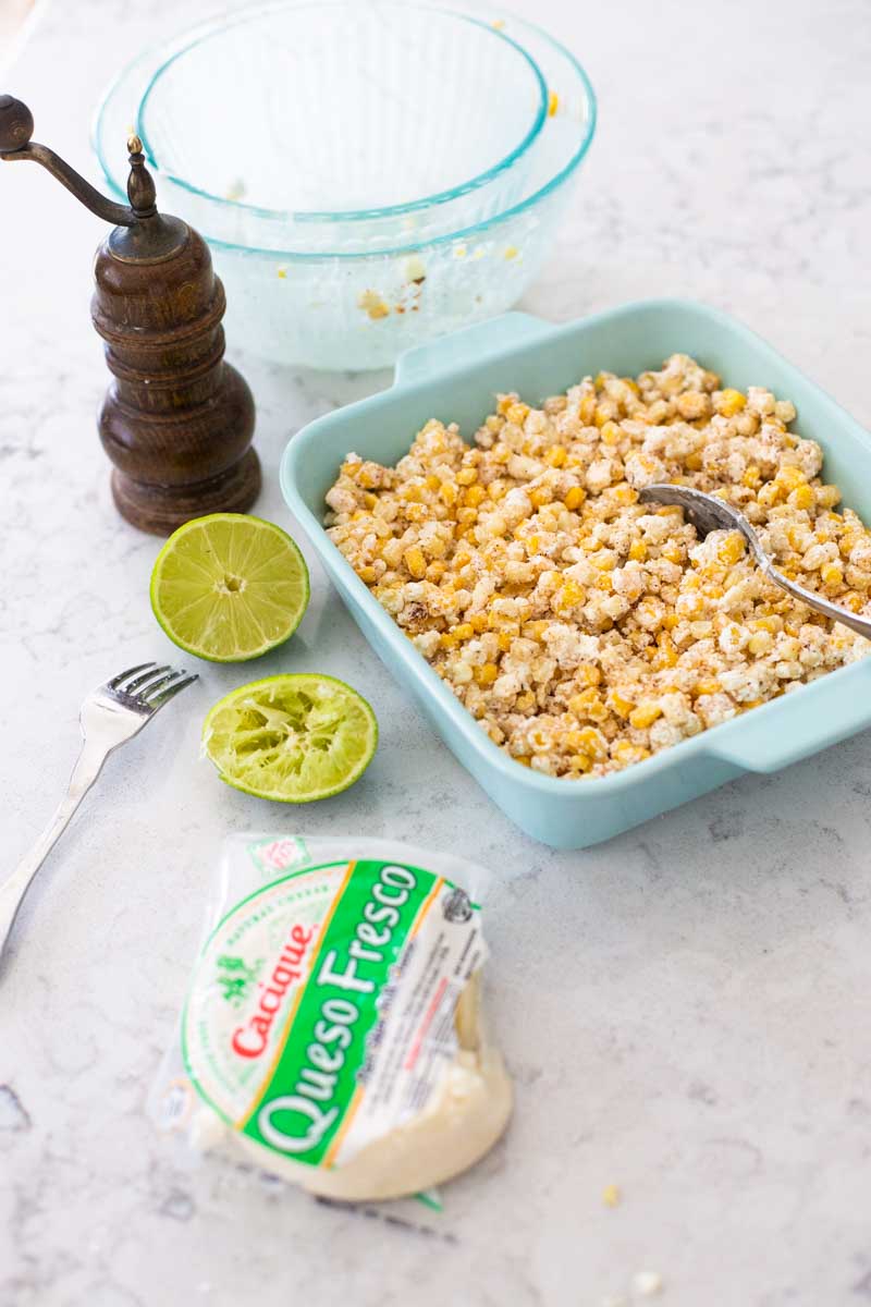 The queso fresco and a fresh lime sit next to a prepared dish of Mexican street corn casserole.