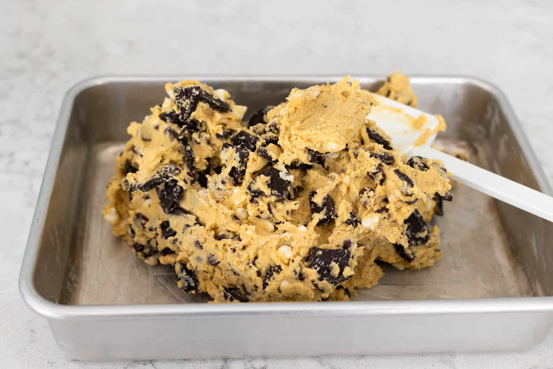The very thick cookie dough is being patted into place in a 9x13-inch baking pan.