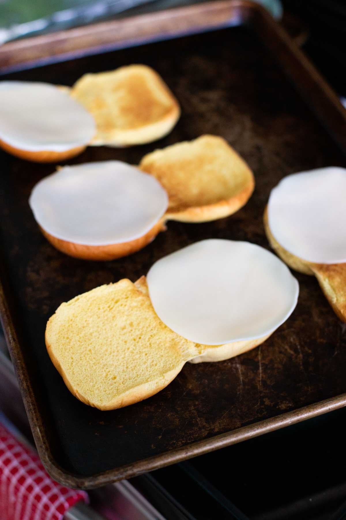 The buns have been toasted on a pan, slices of cheese are now placed on top.