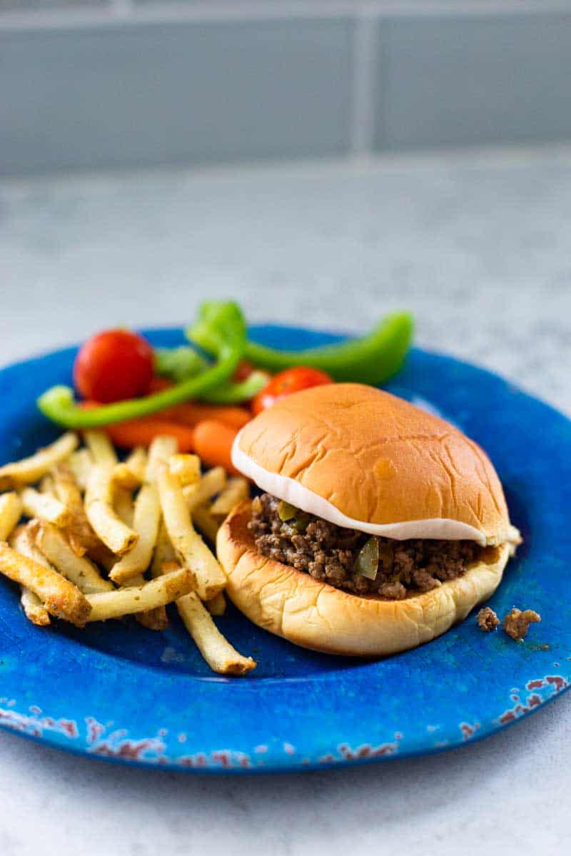 The sandwich is on a blue plate next to some french fries and raw veggies.