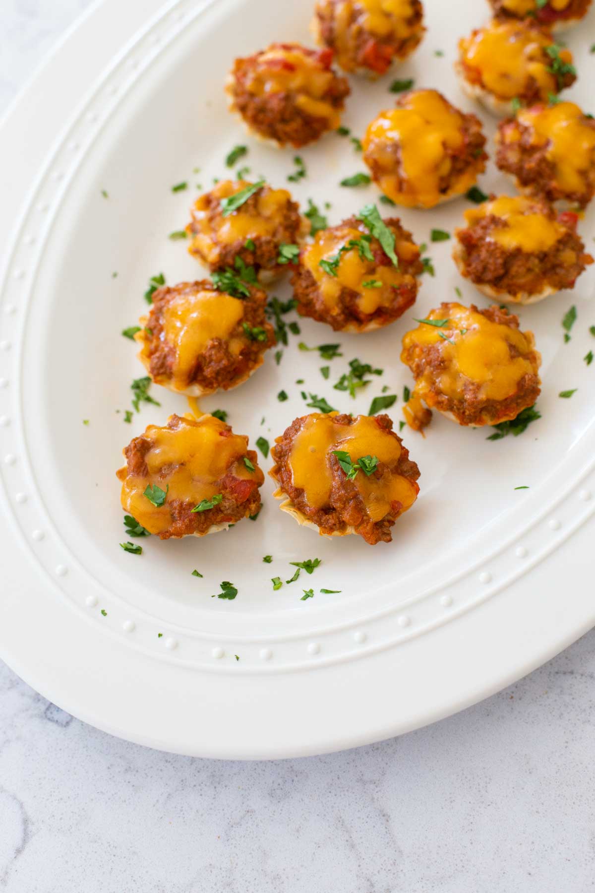 The baked taco bites are served on a white platter and sprinkled with green parsley.