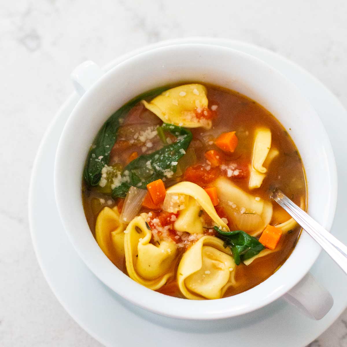 A light and healthy tortellini soup has spinach and carrots floating in the broth.