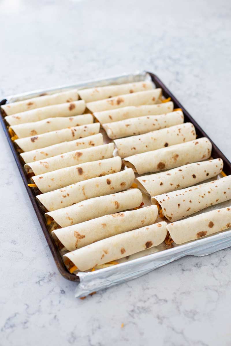 The baking pan shows all the assembled taquitos lined up in neat rows.