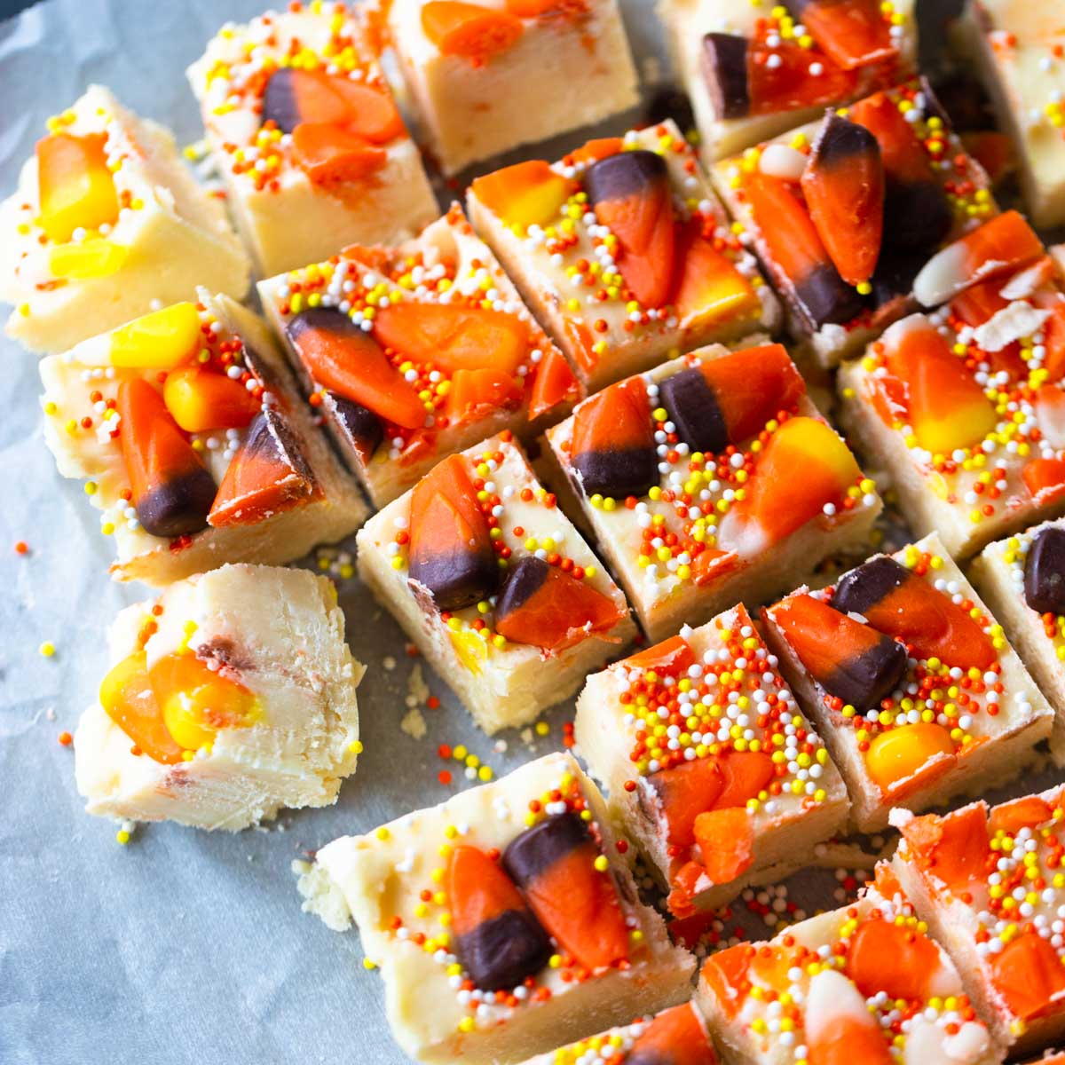 Candy Corn fudge is cut into squares on parchment paper. Orange, black, and yellow candies and sprinkles are pressed into the white fudge.
