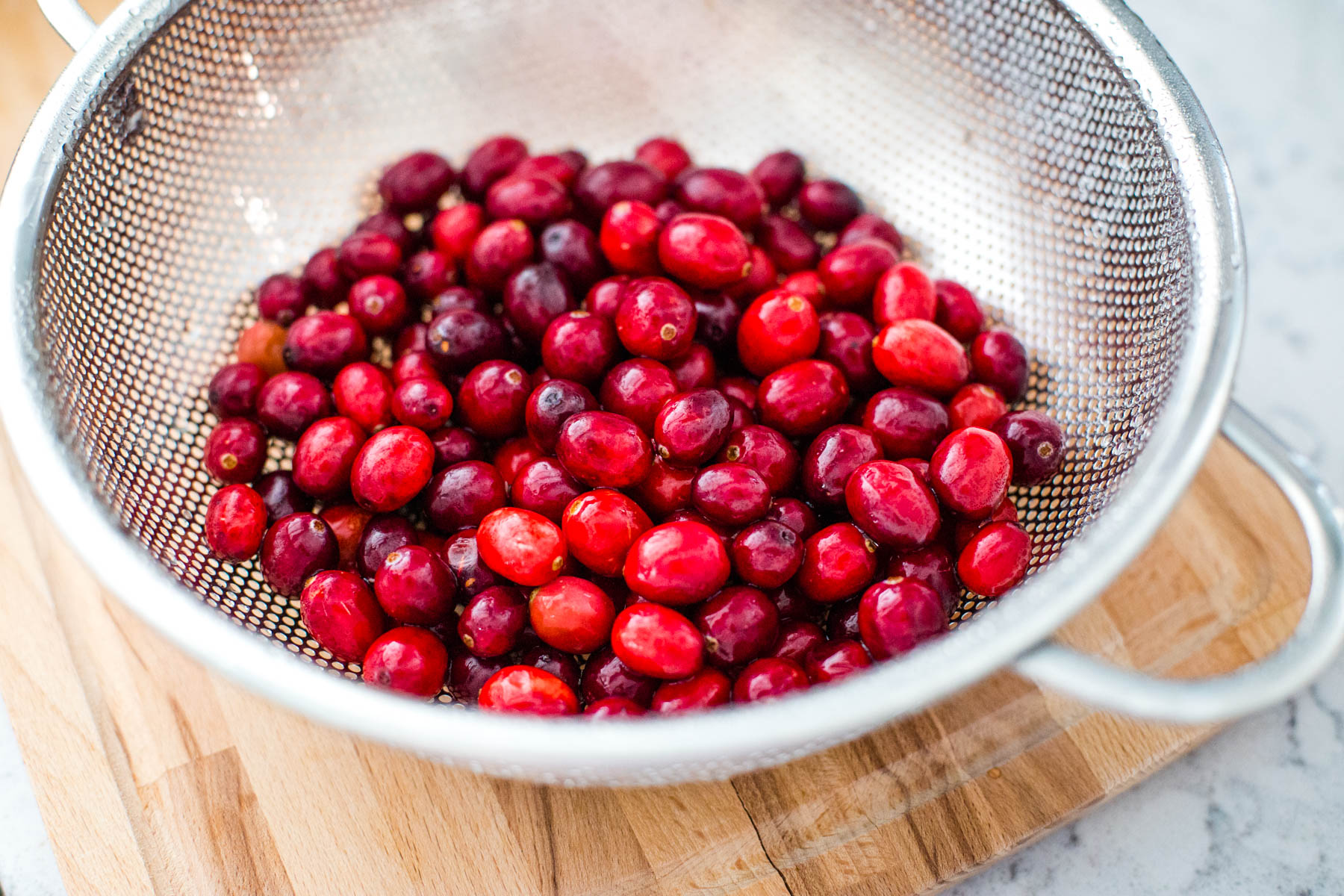 A metal strainer is filled with just-washed fresh cranberries.