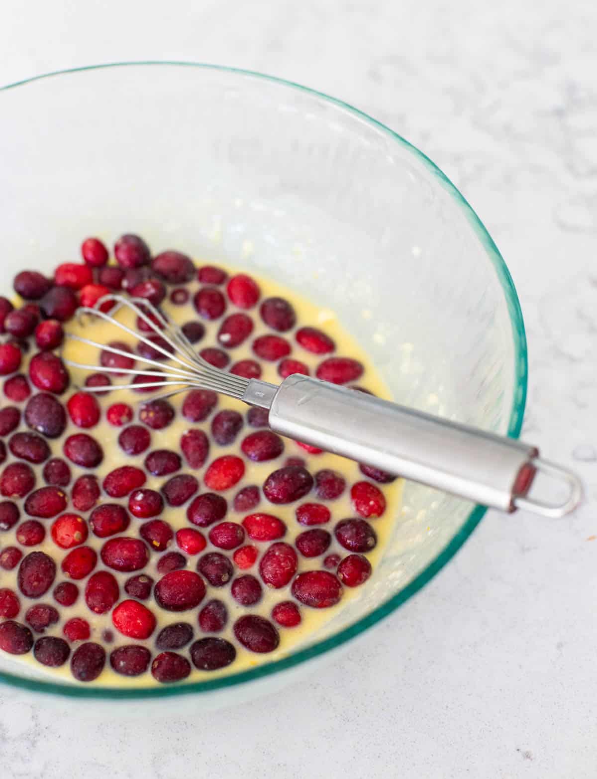 The muffin batter has been whisked together in a mixing bowl. The fresh cranberries are floating on top.