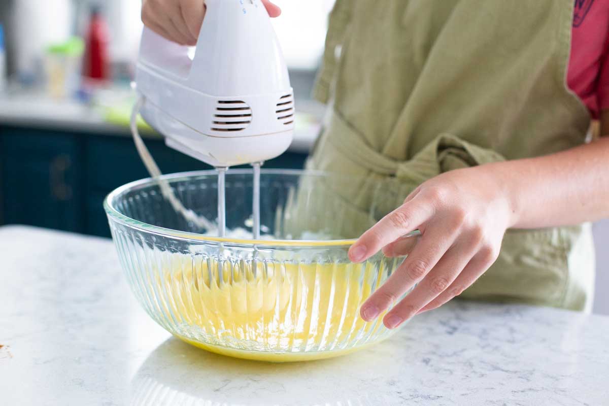 A hand mixer is beating the eggs in a mixing bowl.