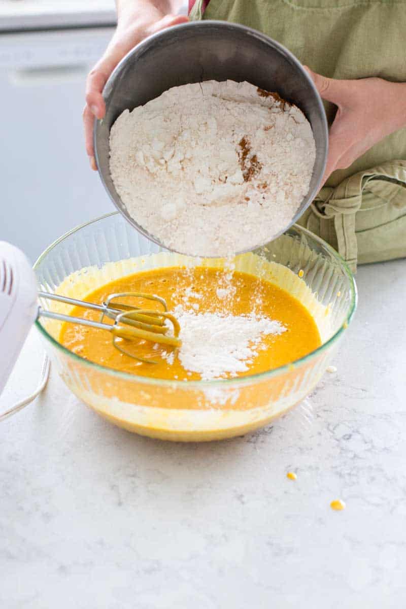 The bowl of flour is being added to the pumpkin mixture.