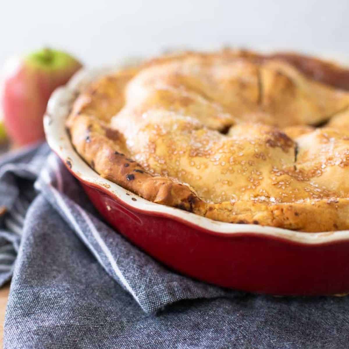 The red ruffled pie dish has an apple pie in it.