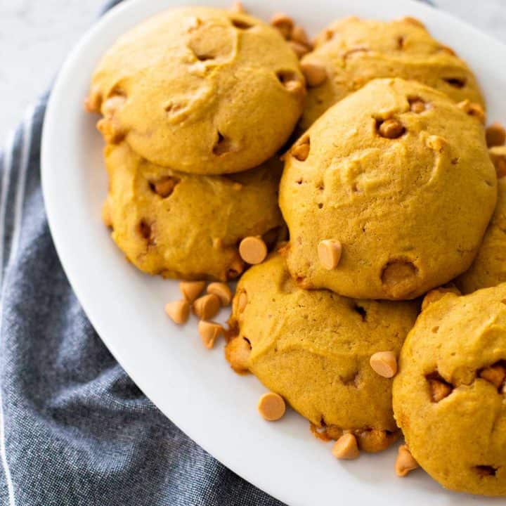 A platter of puffy pumpkin butterscotch cookies with a sprinkle of butterscotch chips sits next to a denim napkin.