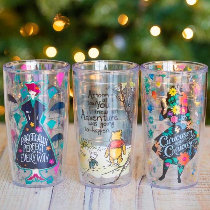 Three Disney themed tumblers on a table in front of a Christmas tree.