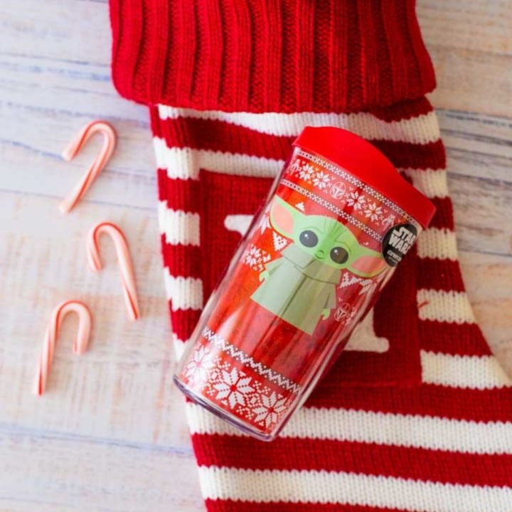 Baby Yoda tumbler sitting on a red and white striped stocking with candy canes.