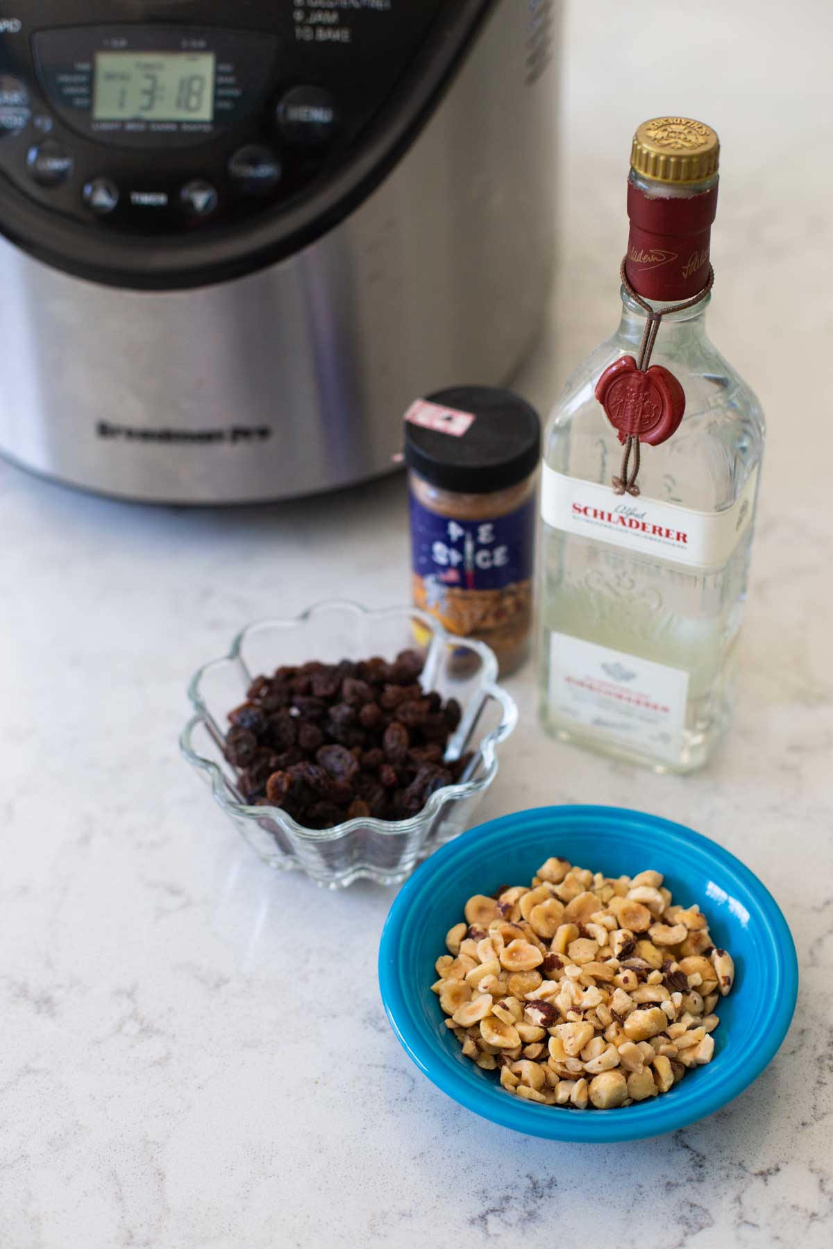 Chopped hazelnuts, raisins, kirsch, and spices sit in front of a bread maker.