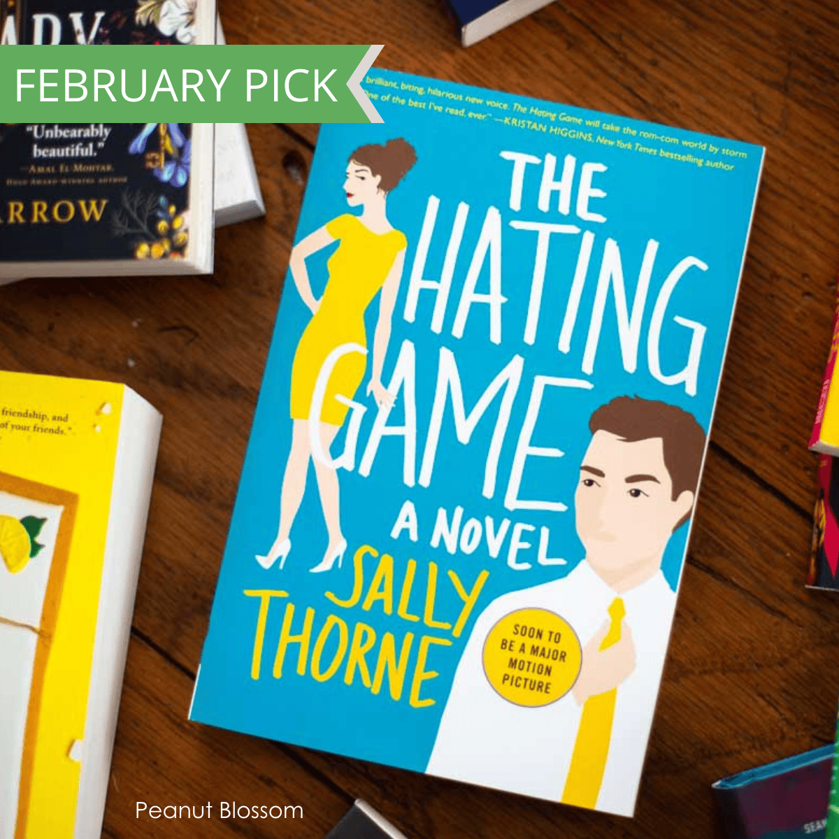 The cover of the book The Hating Game sitting on a table surrounded by other books.