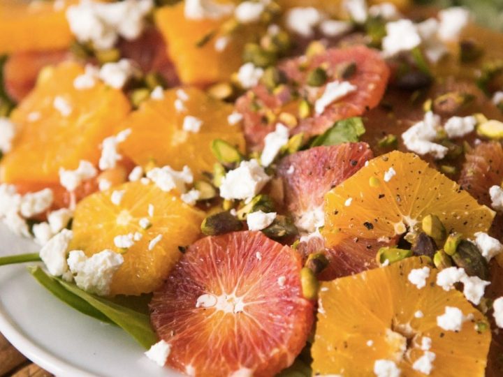 A platter of sliced oranges with crumbled cheese, chopped pistachios, and seasonings.