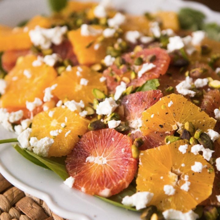 A platter of sliced oranges with crumbled cheese, chopped pistachios, and seasonings.