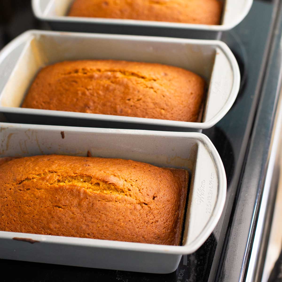 3 pans of homemade pumpkin bread cool on a stove top.
