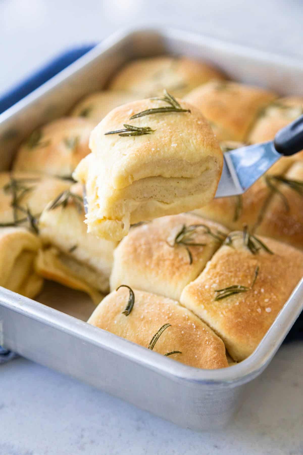 The dinner roll is being lifted out of the pan by a spatula.