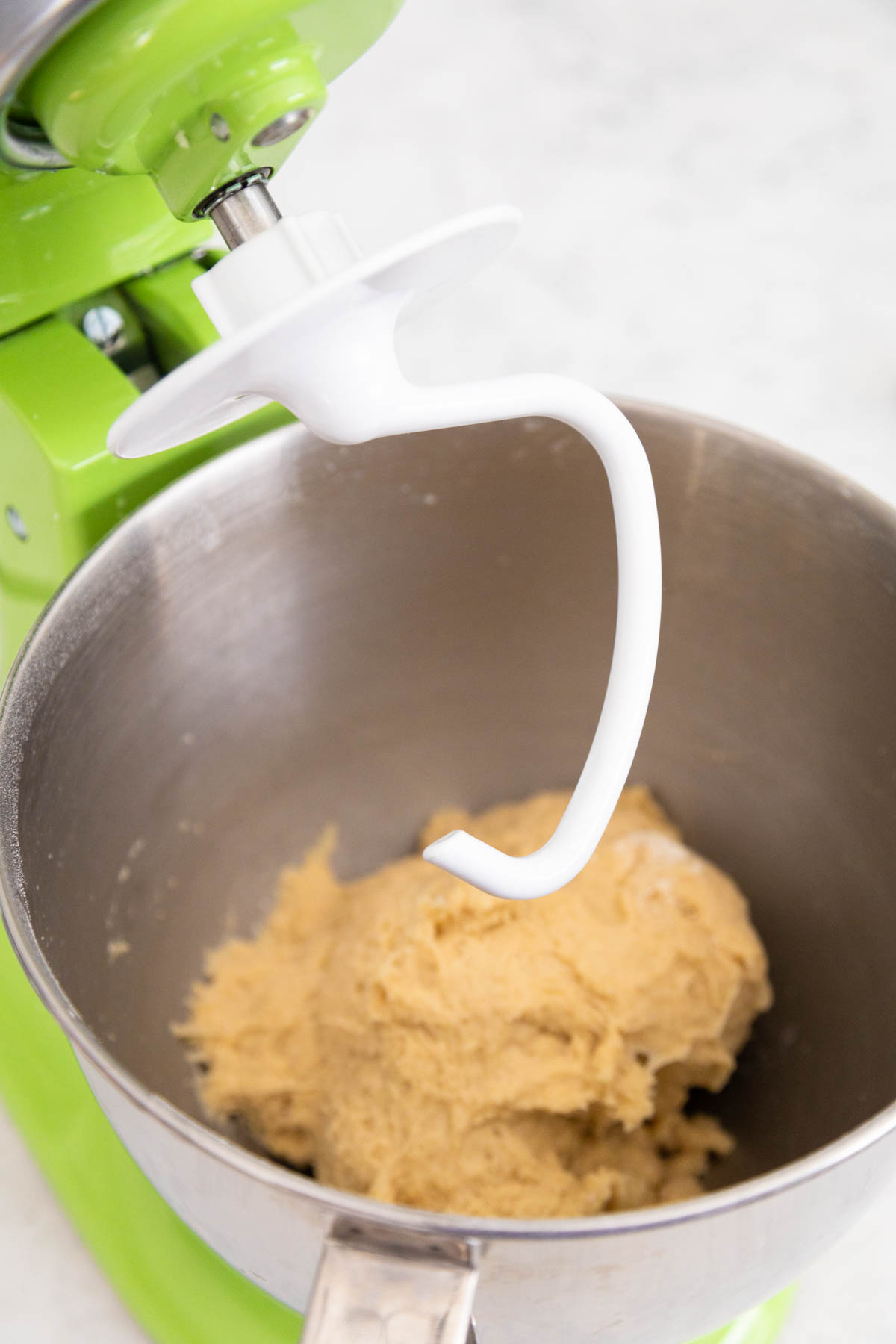 The bowl of the stand mixer has the dinner roll dough and the dough hook is ready to knead it.