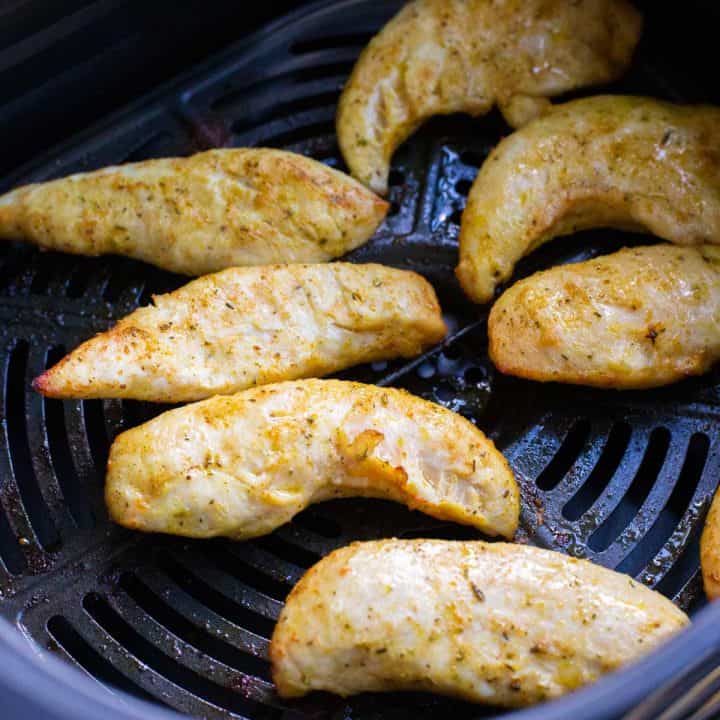 An airfryer basket has 7 seasoned chicken tenderloins golden brown and cooked.