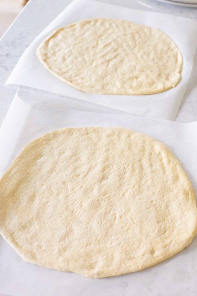 Two pizza crusts are ready to be topped and baked.