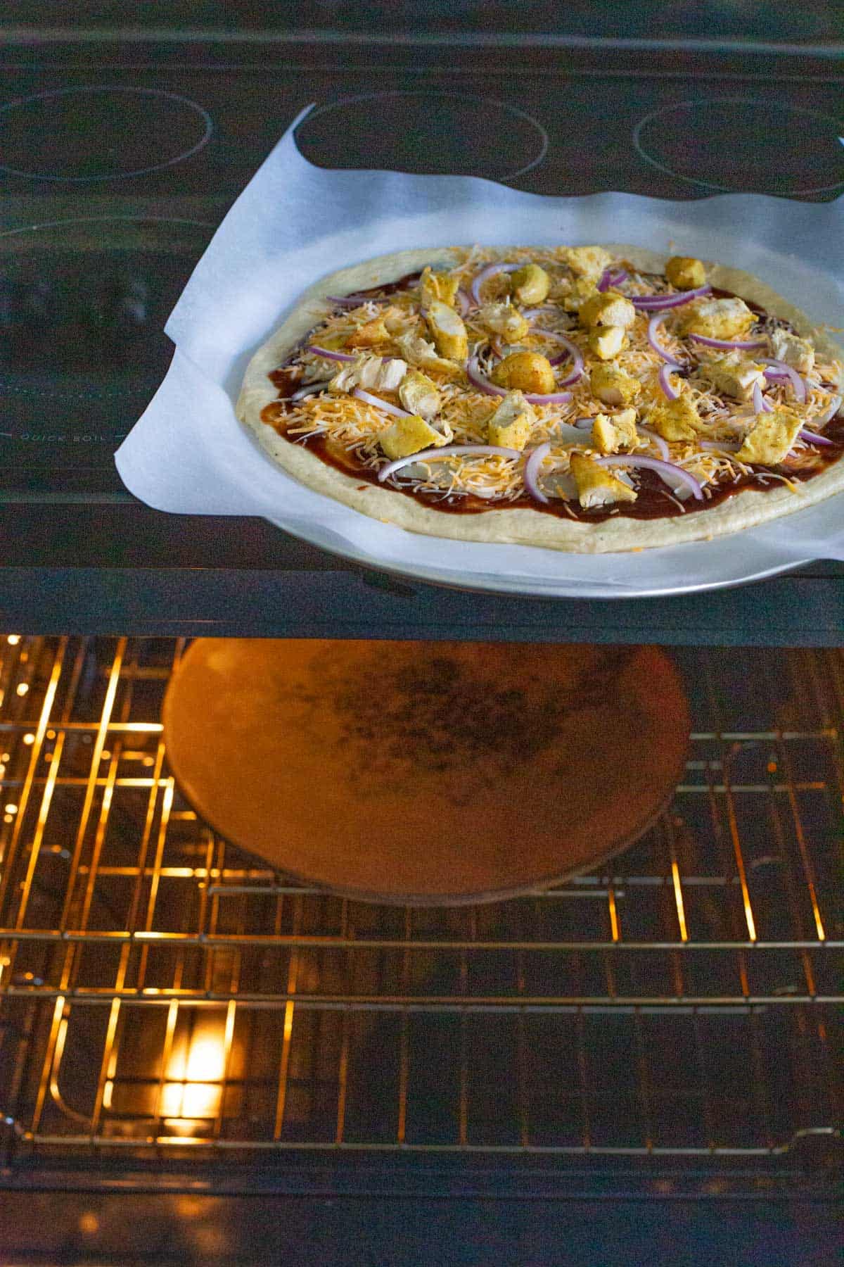 A pizza stone on the center rack of the oven. There's a pizza on the stovetop.