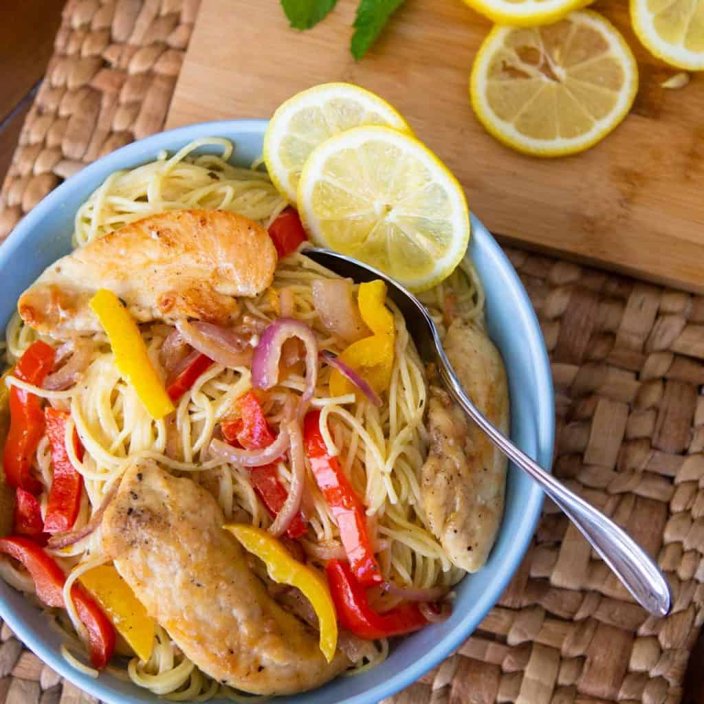 A blue bowl is filled with spaghetti noodles, sliced bell peppers, and chicken tenderloins to show the finished chicken scampi.