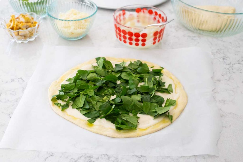 The chicken alfredo pizza has been covered with fresh baby spinach.