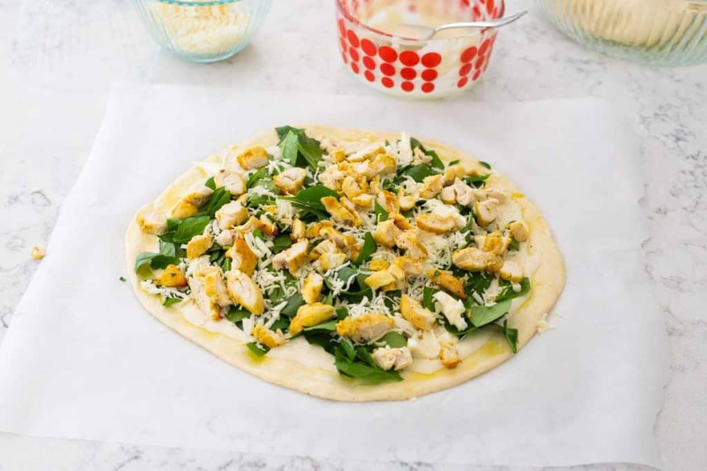 Chicken alfredo pizza has chopped cooked chicken and shredded cheese sprinkled over the top.