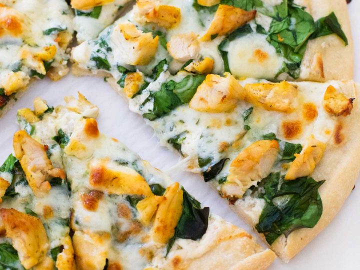 A homemade chicken spinach alfredo pizza has been sliced and the pieces pulled apart.