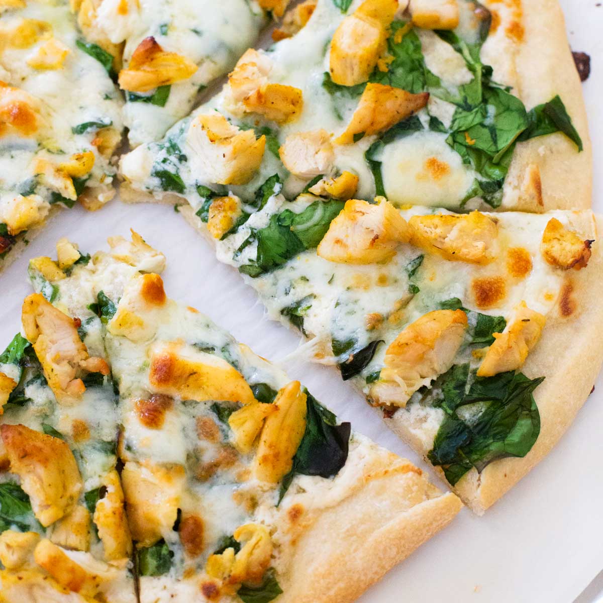 A homemade chicken spinach alfredo pizza has been sliced and the pieces pulled apart.
